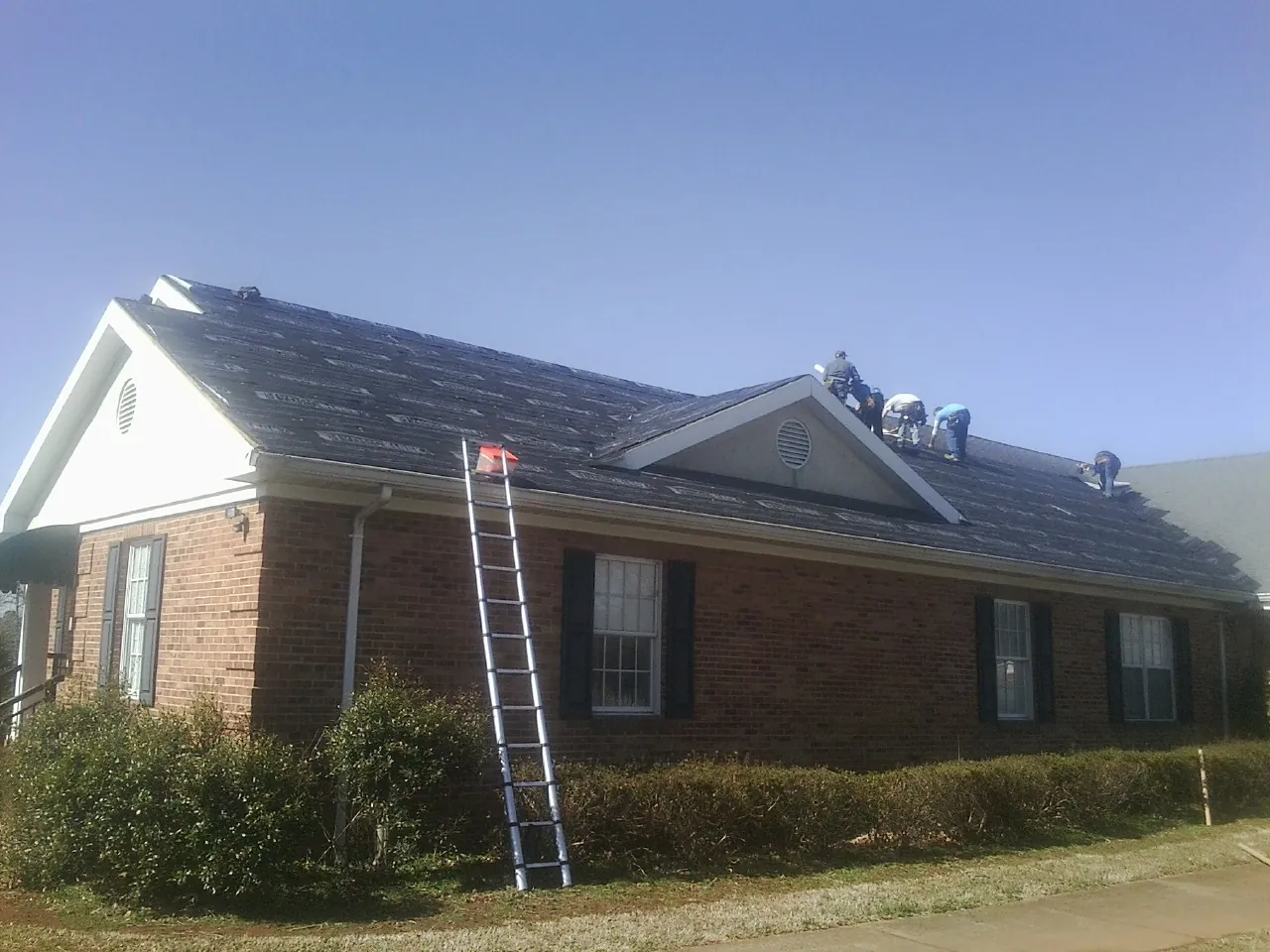 Crew tearing shingles off a brick ranch roof with a ladder set — Emergency Roof Repair work by our crew in Votaw
