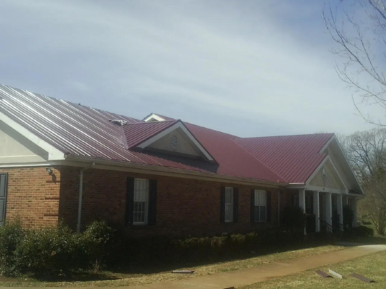 Red metal roof with gabled entries on a long brick building, from a Hail Damage Roof Repair job in Votaw