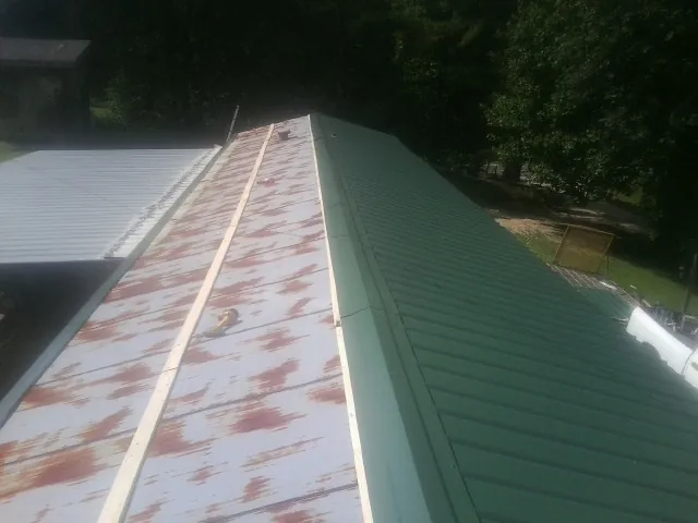 Old rusted panels beside newly installed green metal roofing — Wind Damage Roof Repair by Roofing Brothers in Votaw
