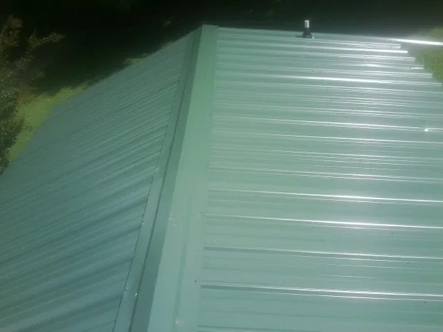 New green metal panels meeting at the ridge of a roof — Flat Roof Repair work by our crew in Votaw
