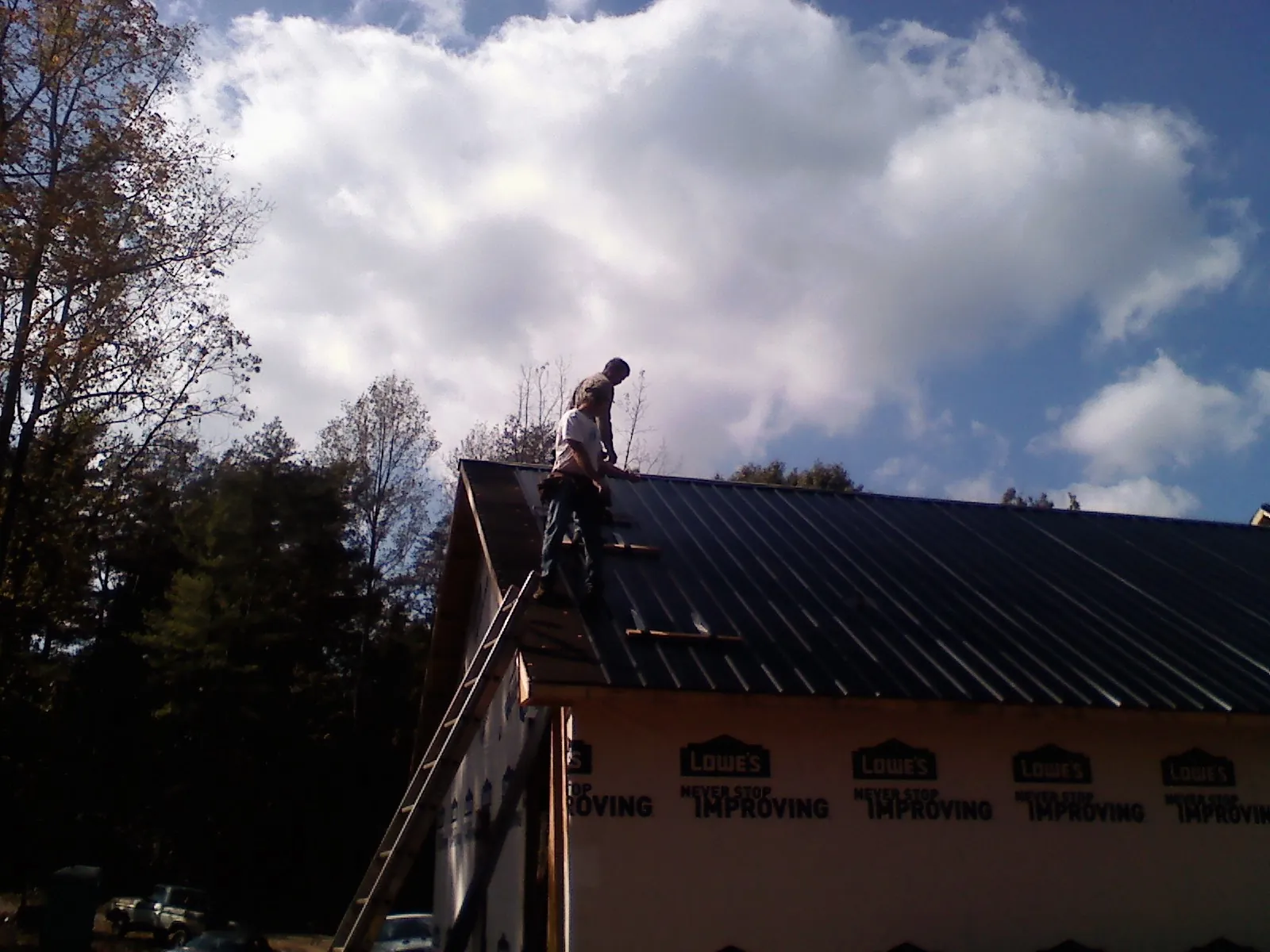 Roofer fastening dark metal panels high against a cloudy sky, from a Roof Inspection job in Votaw