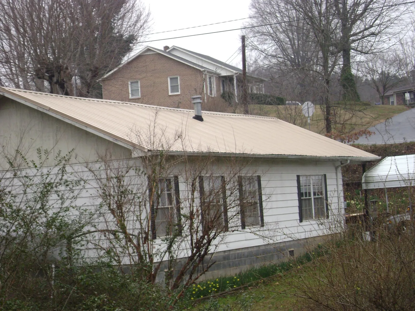 Tan metal roof on a white sided house set into a hillside — Commercial Roofing by Roofing Brothers in Votaw