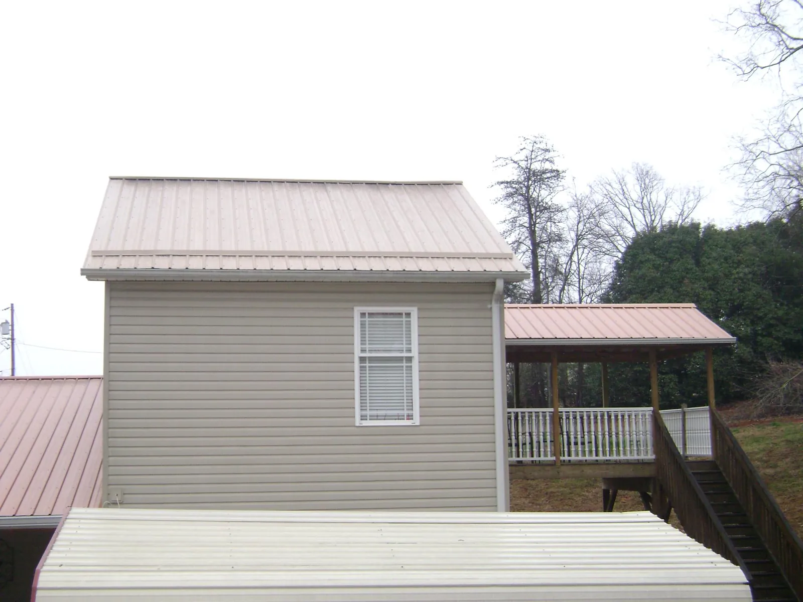 Tan metal roofs on a two story addition and attached porch, from a Roof Replacement job in Votaw